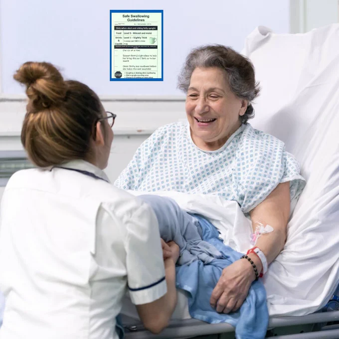 Photograph of a patient sitting in a hospital bed and talking to a member of staff. A green sign can be seen above the patient's bed.