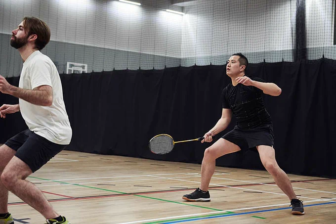 Image of two people on an indoor court, both looking up, as they are playing a game of badminton.