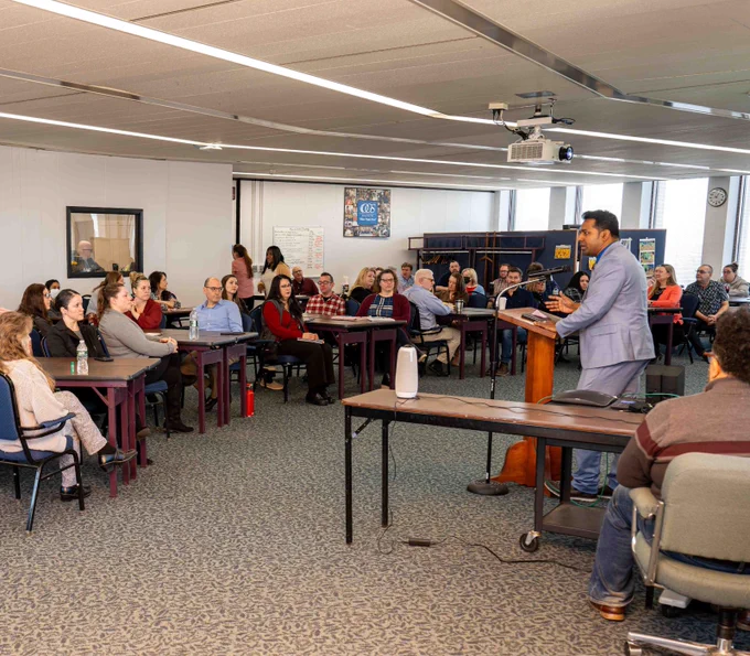 New York State Office of General Services Chief Procurement Officer stands at a podium and speaks to the Procurement Team during a Town Hall meeting. 