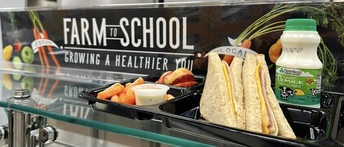 Photo of a lunch tray with a sandwich, milk, carrots, and apple slices.