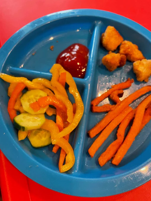 Photo of a blue plate with chicken nuggets, ketchup, sweet potato fries, cucumbers and peppers.