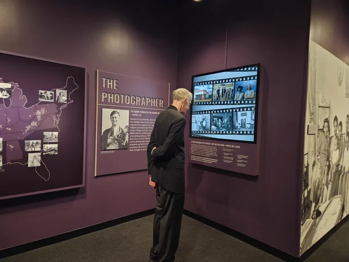 A man looks at an exhibit panel with other panels and large images surrounding him.