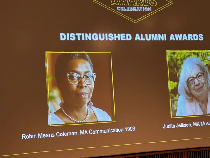 An image of the slide honoring A&S distinguished alumni. Dr. Coleman is being awarded who was earned their MA in Communication department in 1993. She faces the camera with turtle glasses and pearls.