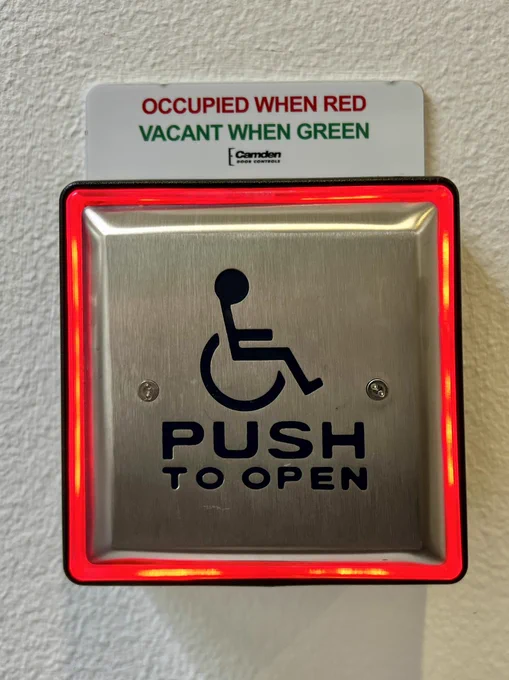 Restroom door “push to open” button with an illuminated border. Sign above says in red “occupied when red” and says in green “ vacant when green”