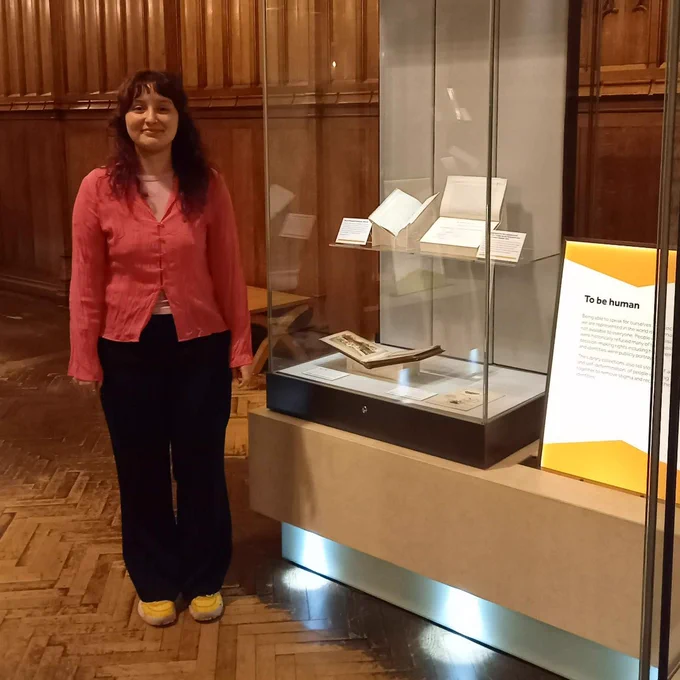 Matilda Seymour-Lewis in the Rylands Gallery standing beside an exhibition case for the We Have Always Been Here exhibition.