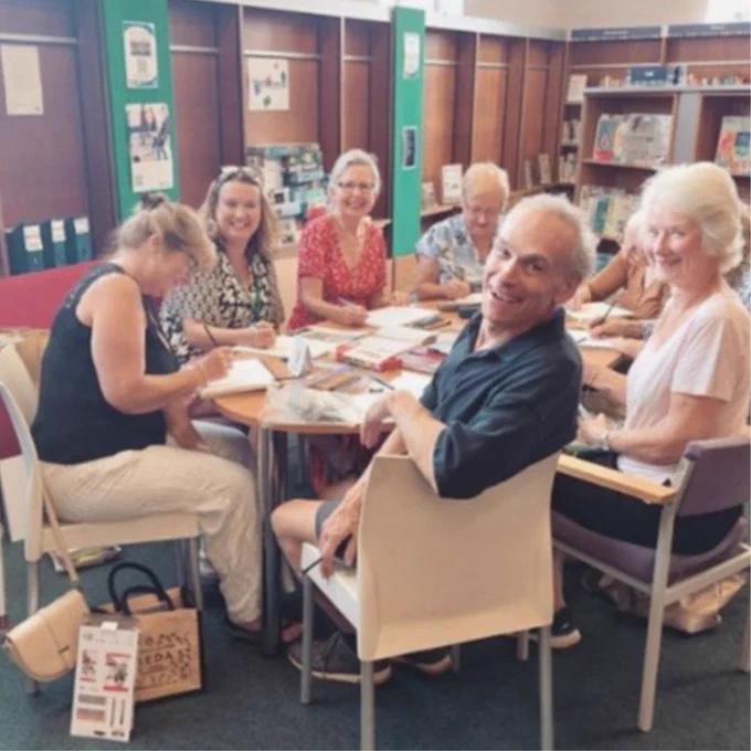 Photo from a library event, with attendees smiling at the camera. The atmosphere looks positive, warm, and welcoming.