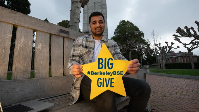 student sitting down smiling at camera holding oversized yellow star with text big give hashtag berkeley B S E 