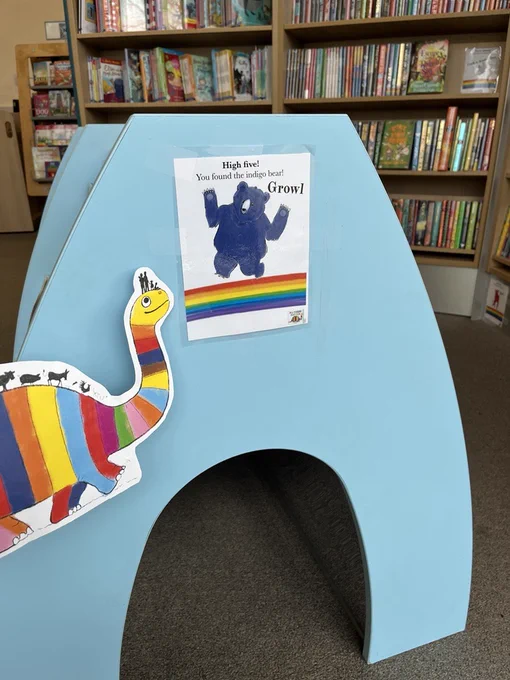 a rainbowsaurus who's just found the indigo bear hidden on the side of the picturebook tunnel in the library