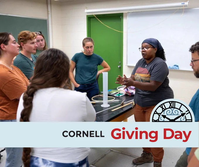 A doctoral student explains an activity to other students. Text reading Cornell Giving Day.