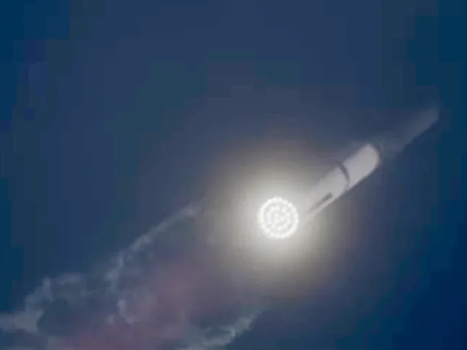 The building-sized SpaceX Starship rocketing toward space at a 45 degree angle on screen. All 33 Raptor engines can be seen burning and a colorful plume of exhaust trails behind.