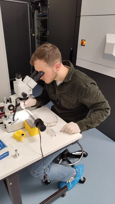 A researcher looks through a microscope at a TEM sample holder in a laboratory.