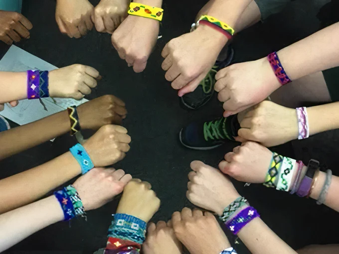 Poignets d’enfants formant un cercle et parés de bracelets et de bijoux tissés sur métier.