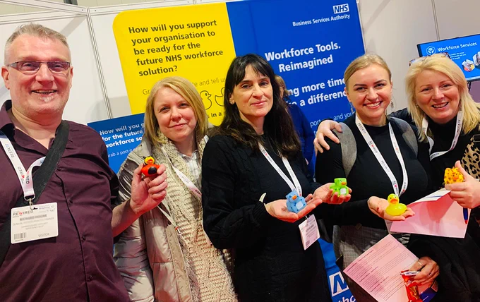 NHSBSA colleagues and visitors at Digital Health Rewired in Birmingham, stood in front of the stand holding rubber ducks.