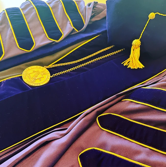 A medal placed on top of a festive purple robe, next to a hat.