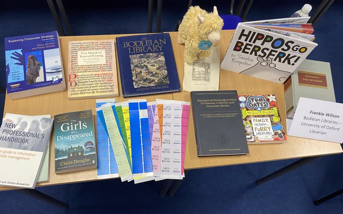 Table with books including “Hippos go berserk” “Exploring corporate strategy” “Benjamin’s sale of goods” “The girls who disappeared” “ Five hundred years of printing”. Also variety of colourful “Facts Matter” stickers and a cuddly alpaca.