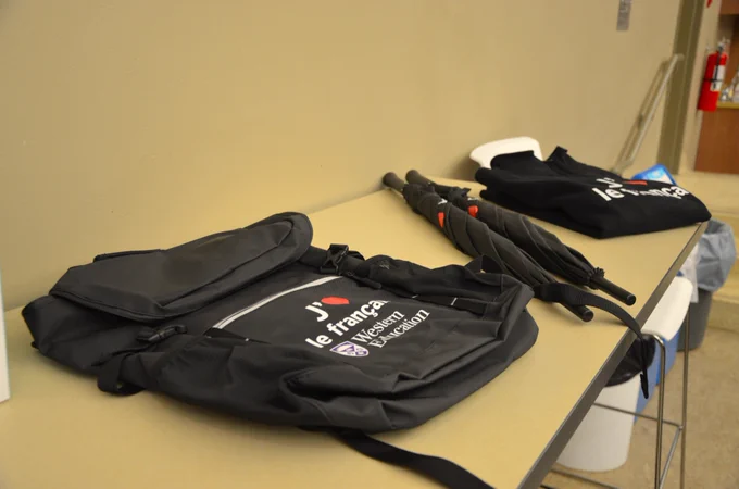 A photo of FSL Western Education merchandise spread across a table. The merchandise includes a backpack, two umbrellas and a half-zip sweater.