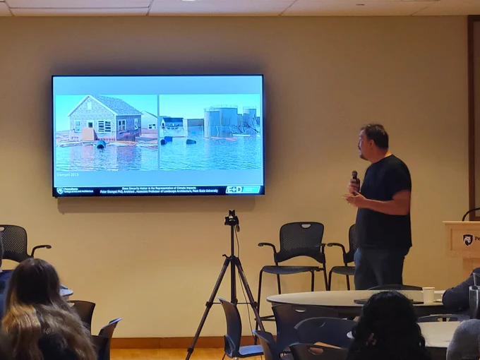 Peter Stempel standing to the right of a slide showing two images. O e is of a house sitting in water surrounded by floating debris.  The second is an industrial site in water with a chain link fence surrounding it and some debris including floating barrels surrounding it. These images were generated using modeling. 