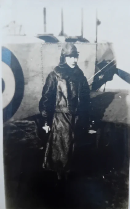 Black and white photograph of a woman in a leather flying suit stood next to the nose of an aircraft with half an RAF roundel showing. 