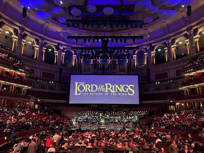 Photo taken from my seat of the round interior of the Royal Albert Hall and rows and rows of seats on all levels. The focus is a large screen in the centre of the stage which has a purple background and gold text reading: The Lord of the Rings: The Return of the King