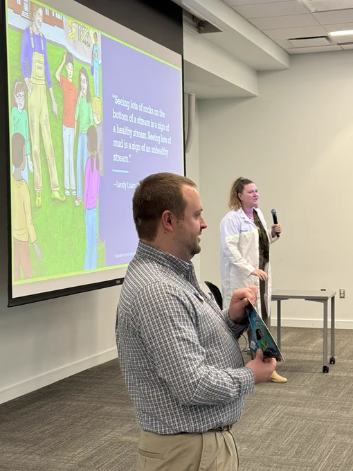 Two people presenting the Brooke meets a stream doctor booklet. 