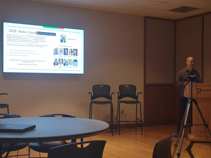 Andy Warner behind the podium beside a slide showing the members of the water council and a brief history of the council which was formed in 2018. 