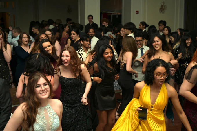 A large group of people smiles and dances in a ballroom.
