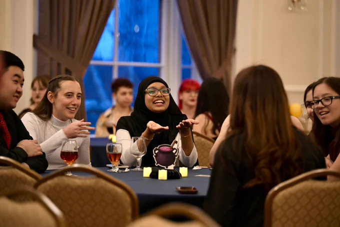 A group of students sits at a table, smiling and talking.
