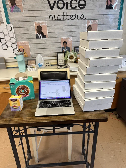 A laptop on a table, alongside a tall stack of pizza boxes.