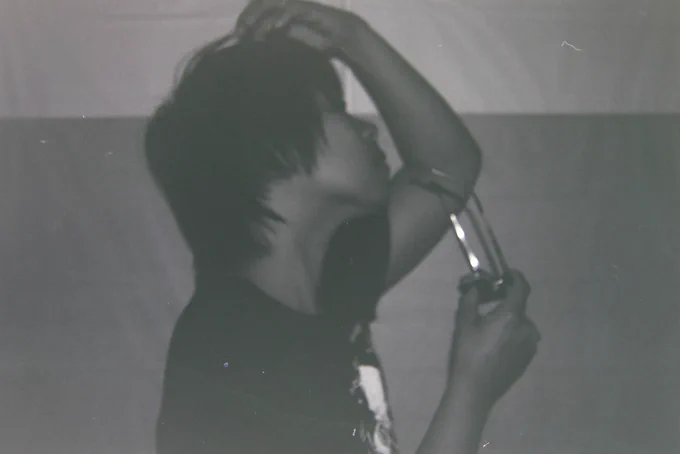 Black and white photo of Sean facing the side, taking off his glasses, while fixing his hair.