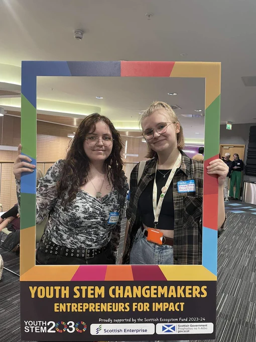 Two people holding up a Youth STEM changemakers frame, smiling at the camera