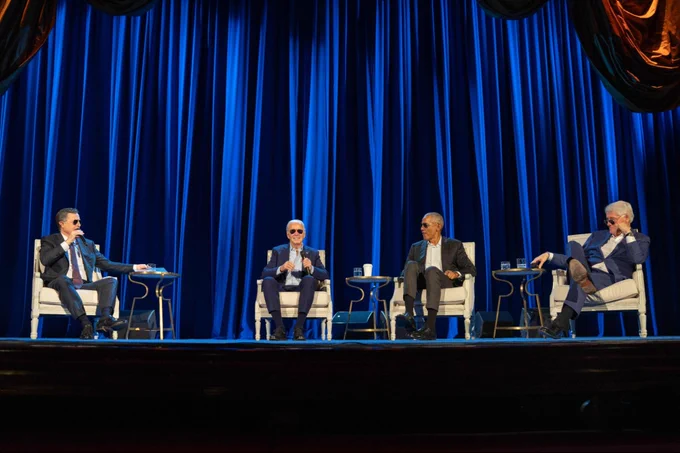 President Joe Biden, Barack Obama, Bill Clinton, and moderator Stephen Colbert sit on stage in Aviator style sunglasses.