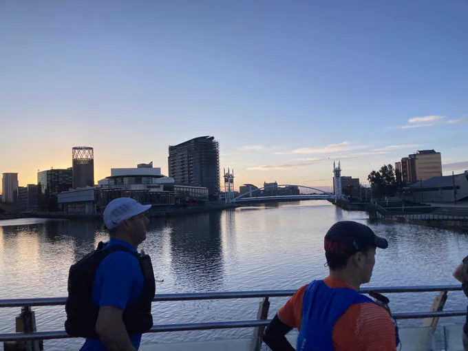 View from bridge across Salford Quays: water in the early morning light with a bridge and buildings in the background. Two runners close to the camera