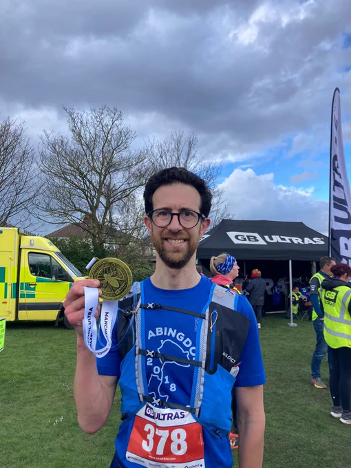 Me holding a large medal, wearing a backpack and with a race number pinned to my T shirt