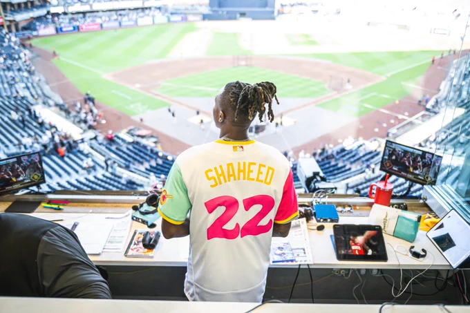 Rashid Shaheed standing in one of the Padres' broadcast booths and looking out at the field at Petco Park. He is wearing a custom Padres City Connect jersey that has his last name on the back (Shaheed) and the number 22 (the same number he wears on the Saints).
