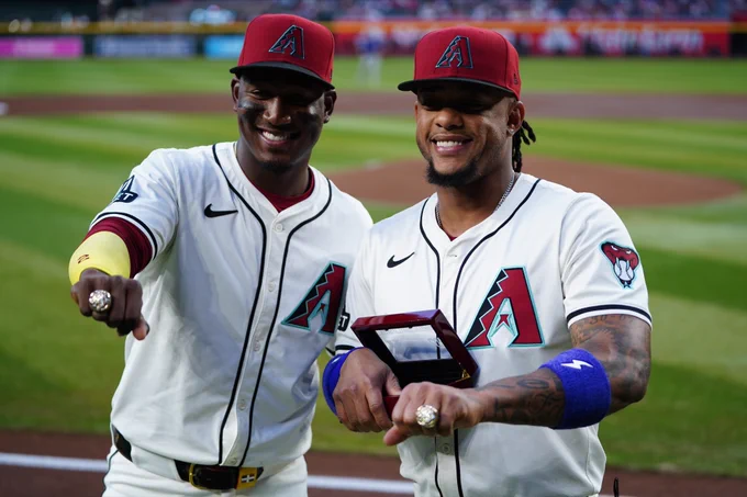 Geraldo Perdomo (left) and Ketel Marte (right) wear their 2023 National League Championship rings. Both wear home white Arizona Diamondbacks uniforms and brick red Arizona Diamondbacks hats.