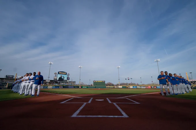 Wide angle photo from behind home plate of two baseball teams lined up for the national anthem 