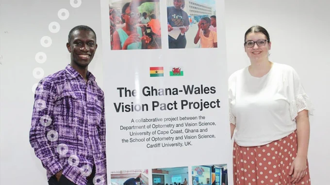 A man and a woman standing either side of a poster to promote the Ghana-Wales Vision Pact Project. 