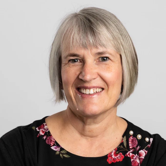 Woman with grey hair smiling wearing black top with pink flowers 