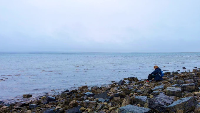 Woman on a rocky beach recording sound of the sea.
