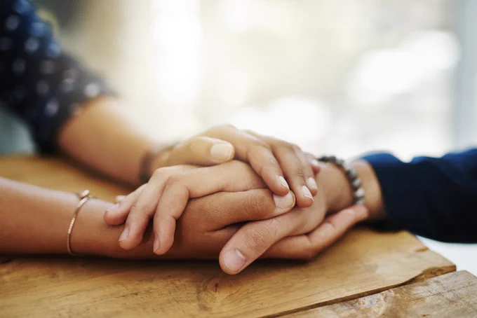 Image: one person's hand rests in another person's hands on a table