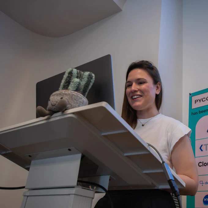 A woman on the podium doing her talk. A plush toy of a cactus sits on the podium