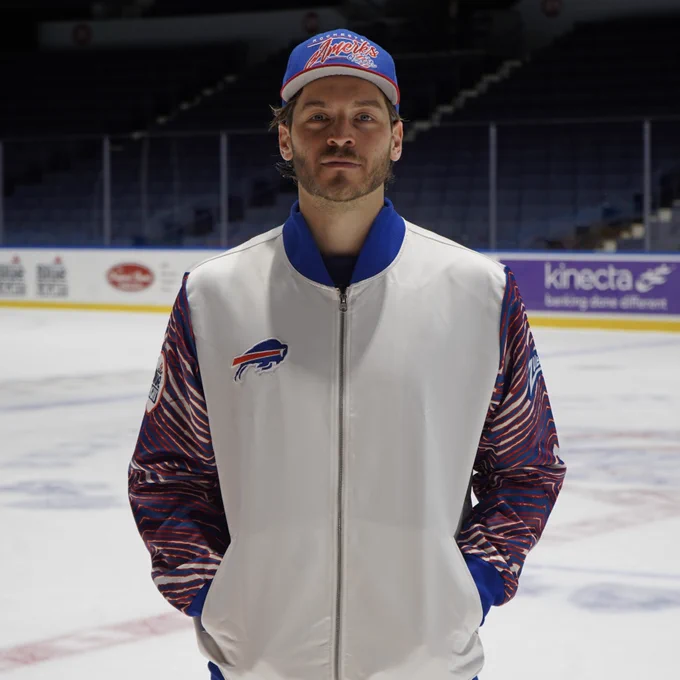 Joseph Cecconi, in a white Buffalo Bills jacket with red and blue striped Zubaz print on the sleeves, stands on the ice and smiles.