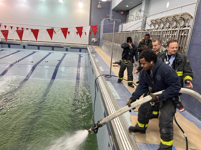 A fire fighter is holding a fire hose spraying water into an empty pool.