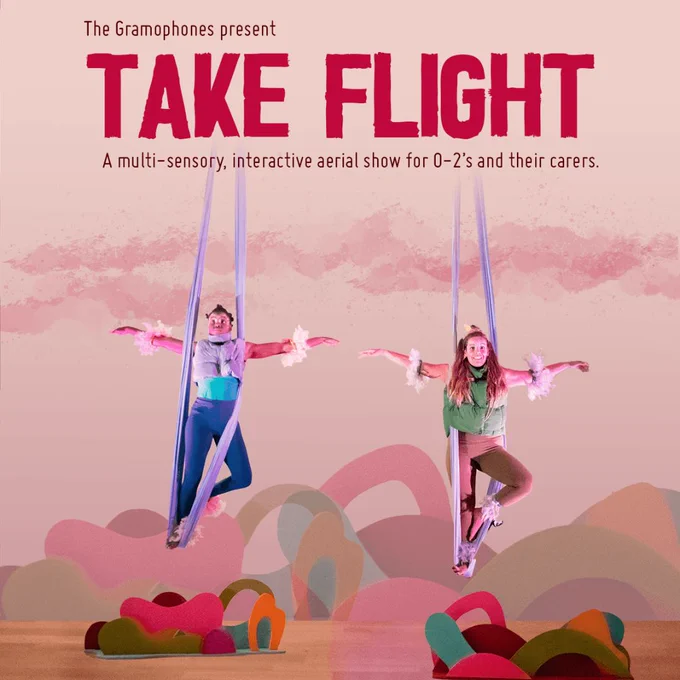 Two people dressed as birds hang in slings with their arms outstretched. Behind them are clouds and colourful shapes. 