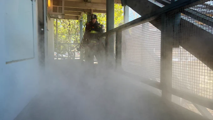 Engineer Schultz in turnout gear carrying a hose over his right shoulder analyzing the smoke on the second floor of one of Solano Park’s units.