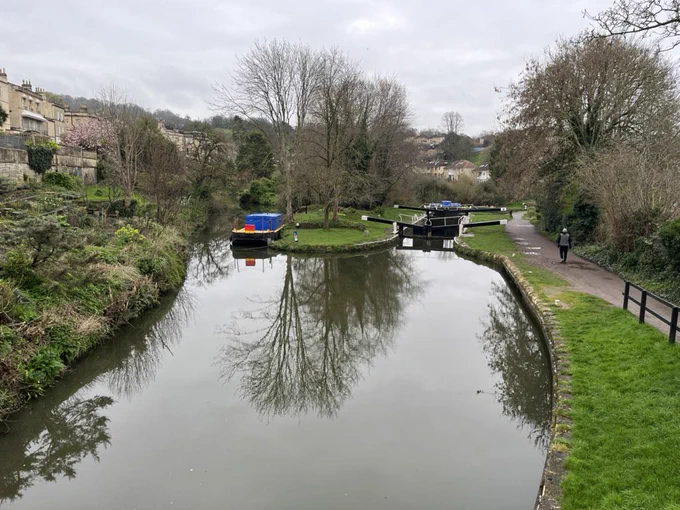 A canal with locks on the right and a canal boat on the left, overlooked by houses.