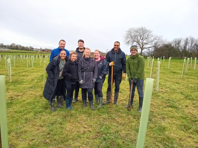 Group of people in a field surrounded by freshly planted trees