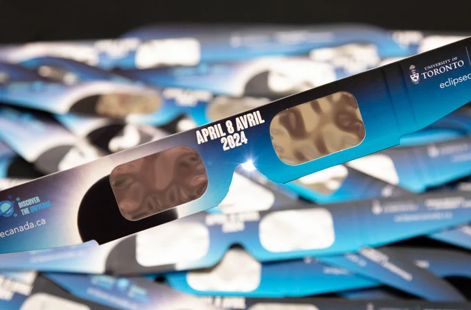Eclipse glasses that say "April 8 2024" in the middle and have the Discover the Universe and University of Toronto logos on the arms.