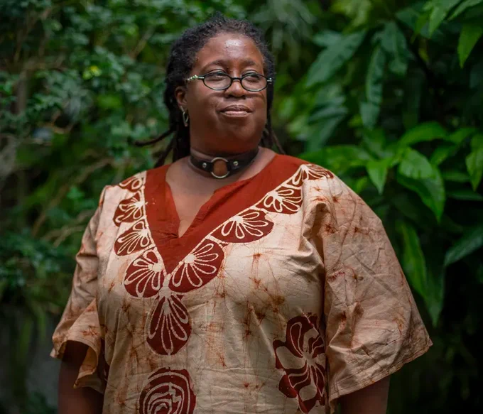 Image of a brown-skinned woman wearing glasses and a brown patterned shirt. 