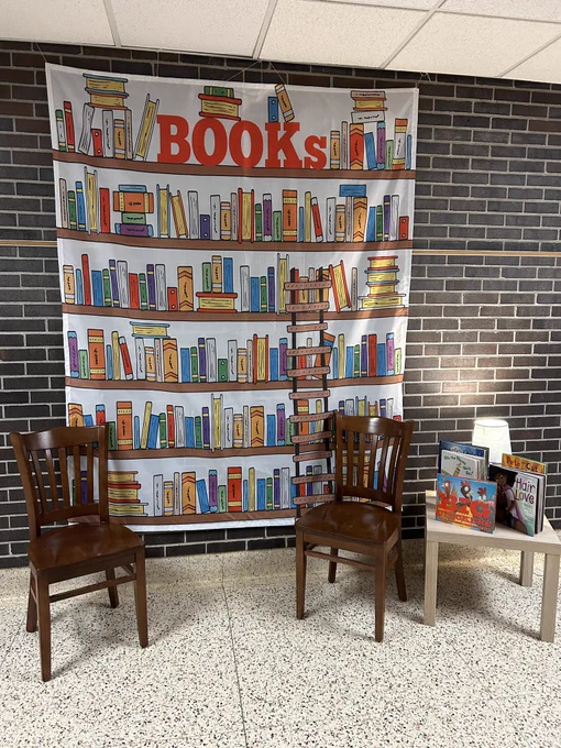 Back drop with a library scene behind two chairs and an end table with books on it